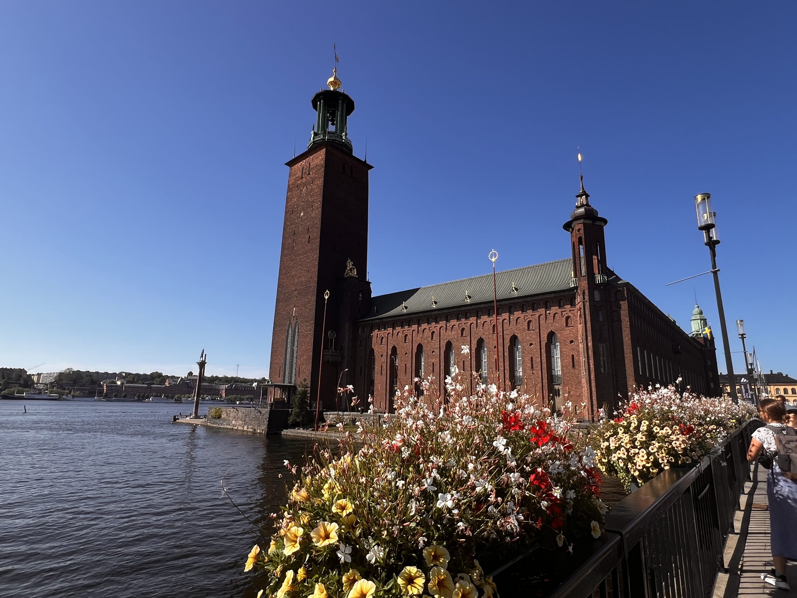 ストックホルム市庁舎の外観、水辺に咲く色とりどりの花と青空が美しい